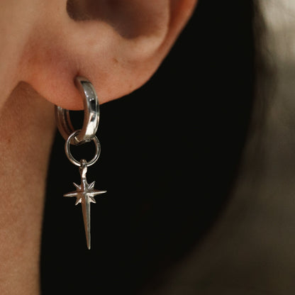 Silver hoop earring with a star-shaped charm worn on an ear.
