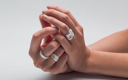 Close-up of hands wearing silver rings on a light gray background