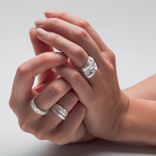 Close-up of hands wearing silver rings on a light gray background