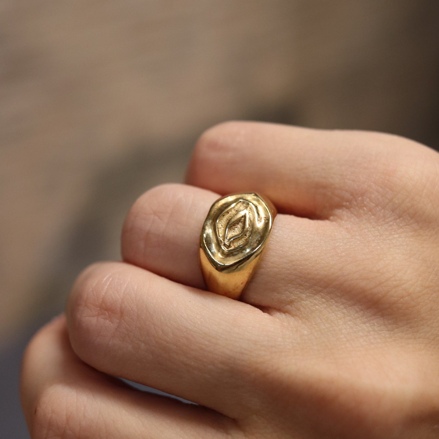 Gold ring with a leaf design on a person's finger against a blurred background