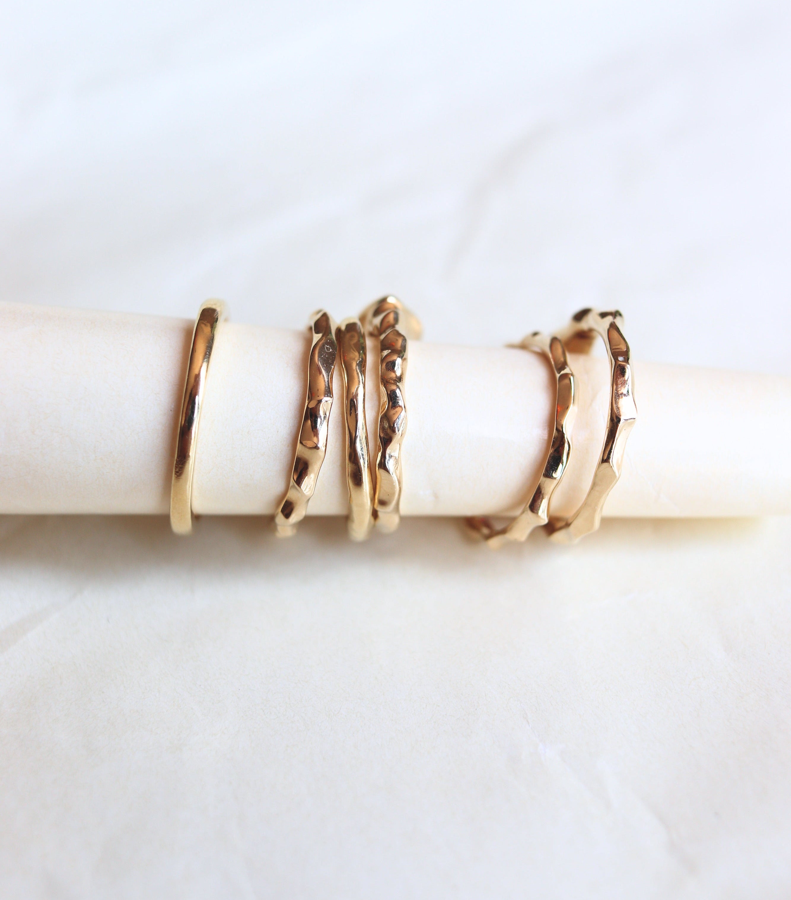 A set of gold rings displayed on a cream-colored ring holder, photographed against a soft white fabric background.