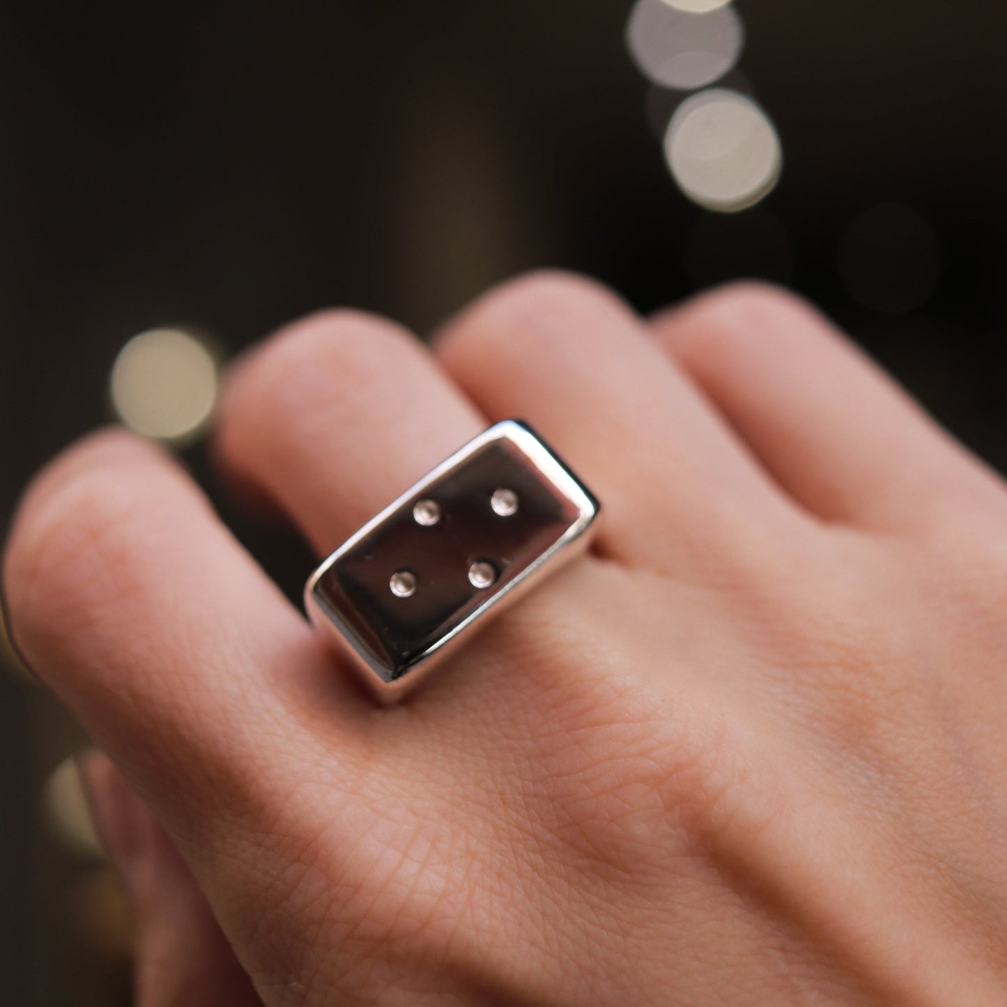 Close-up of a hand wearing a silver ring with three stones against a blurred background