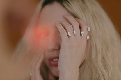 Woman with blonde hair and multiple diamond earrings holding her face.