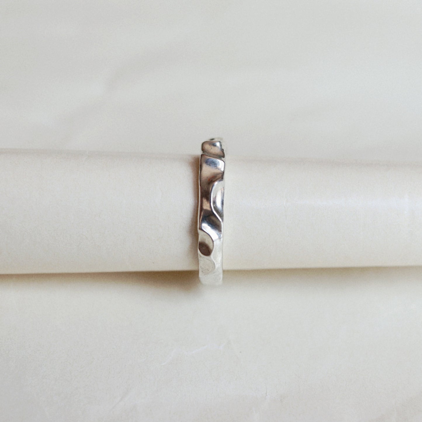 A thin metallic ring with a textured, hammered finish, centered on a wrinkled white paper background.