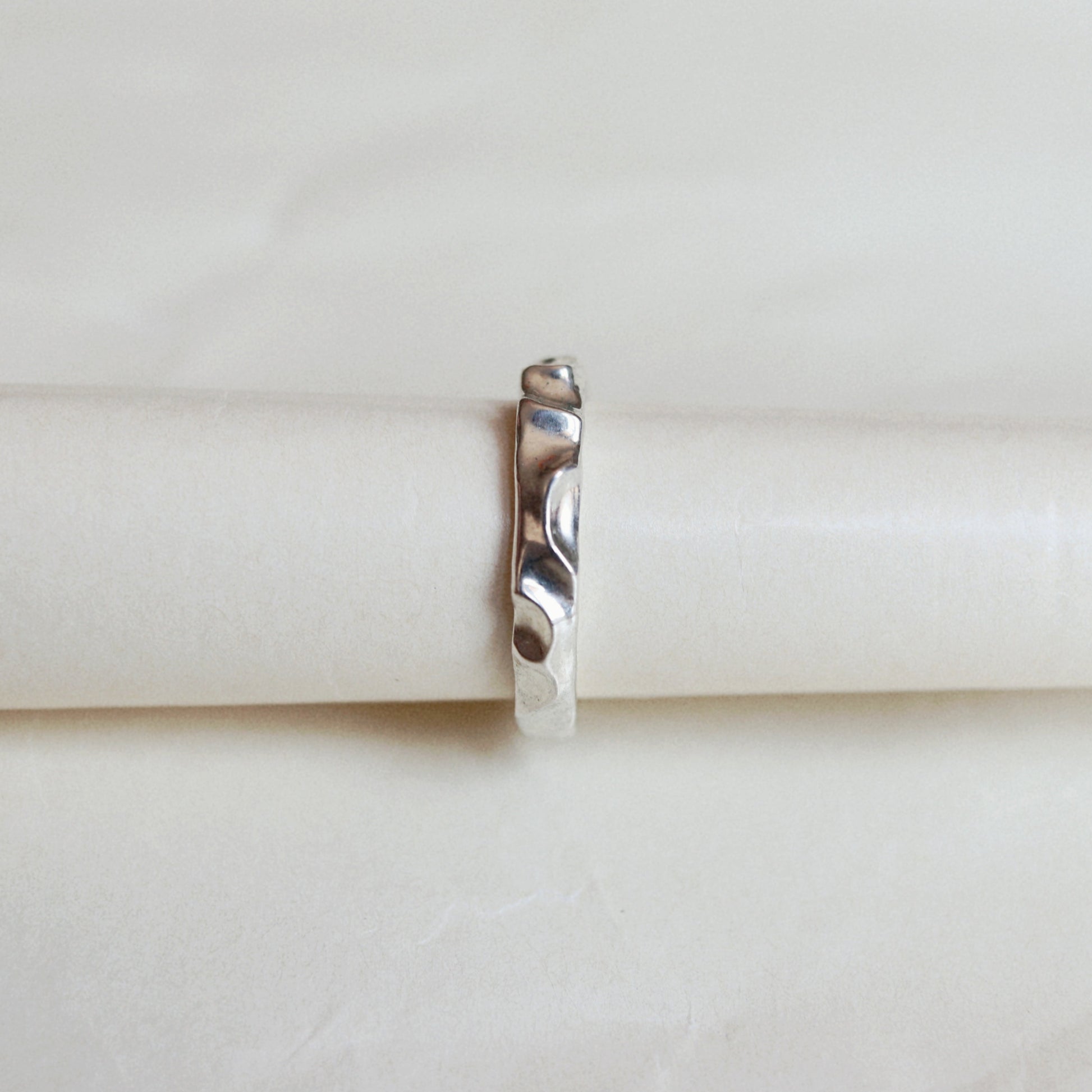 A thin metallic ring with a textured, hammered finish, centered on a wrinkled white paper background.